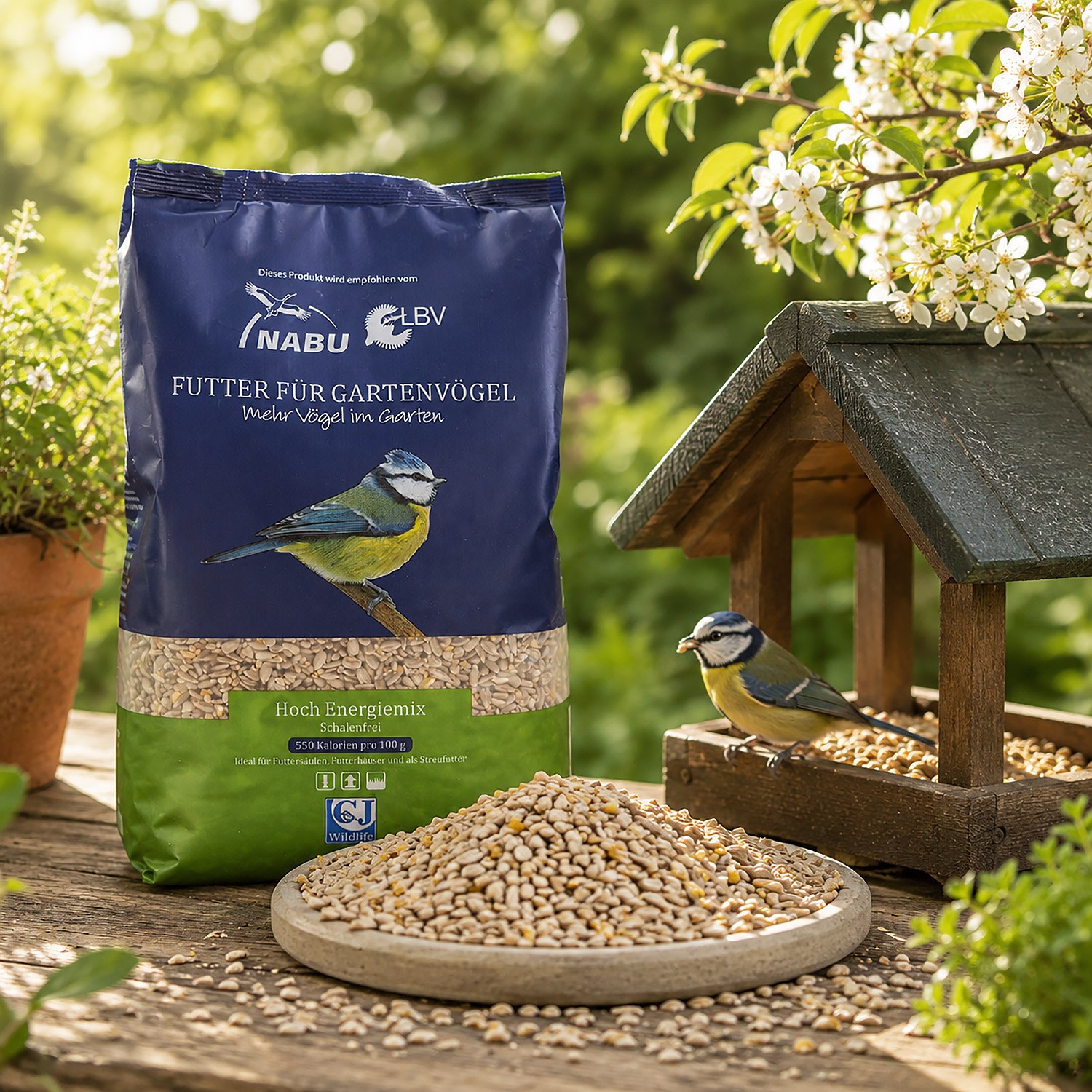 Eine Packung „Futter für Gartenvögel“ neben einer Schale mit Körnern und einem kleinen Vogelhaus, an dem zwei Meisen sitzen.