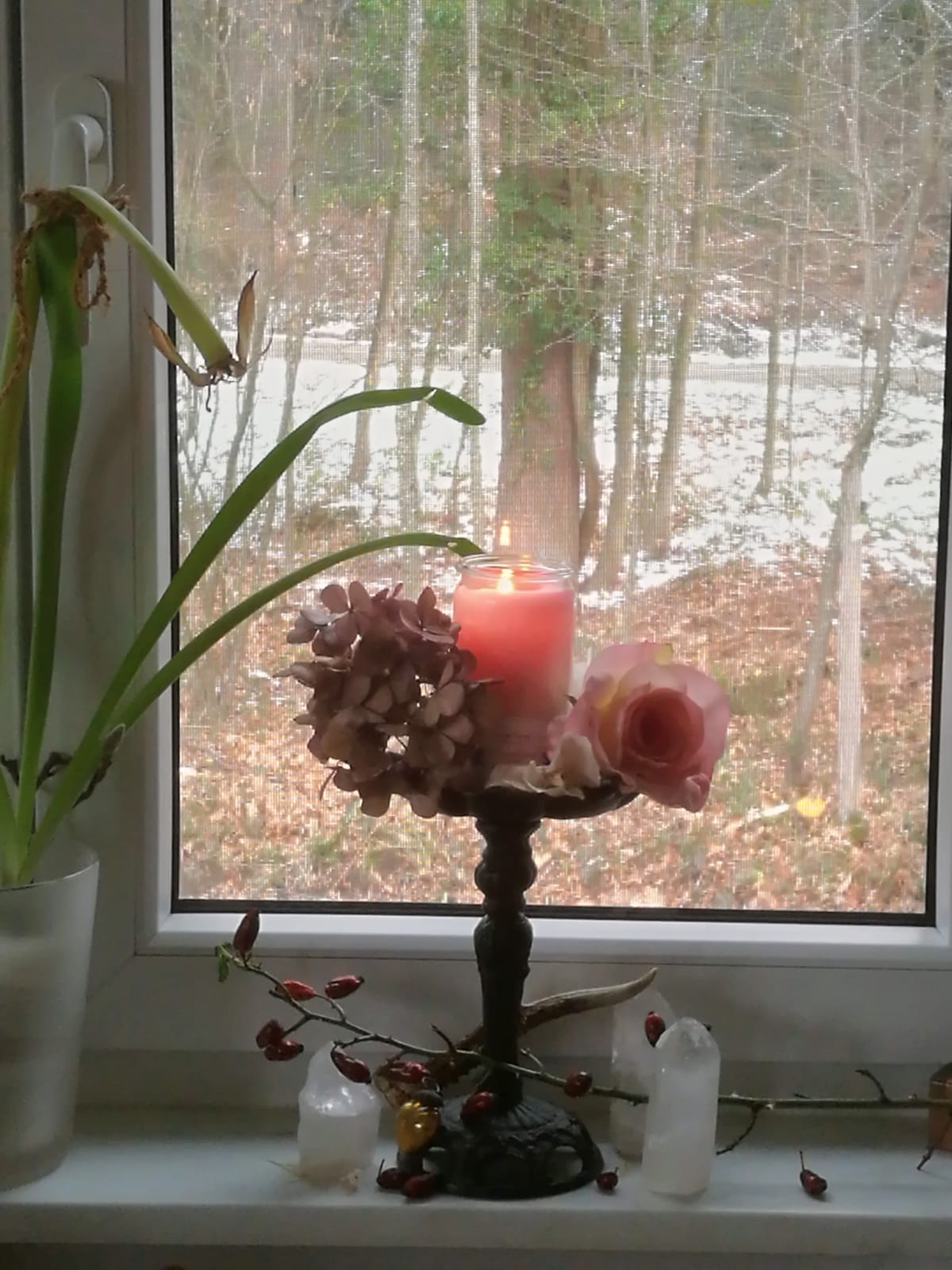 Brennende Kerze auf einem mit Blumen geschmückten Kerzenhalter auf einer Fensterbank