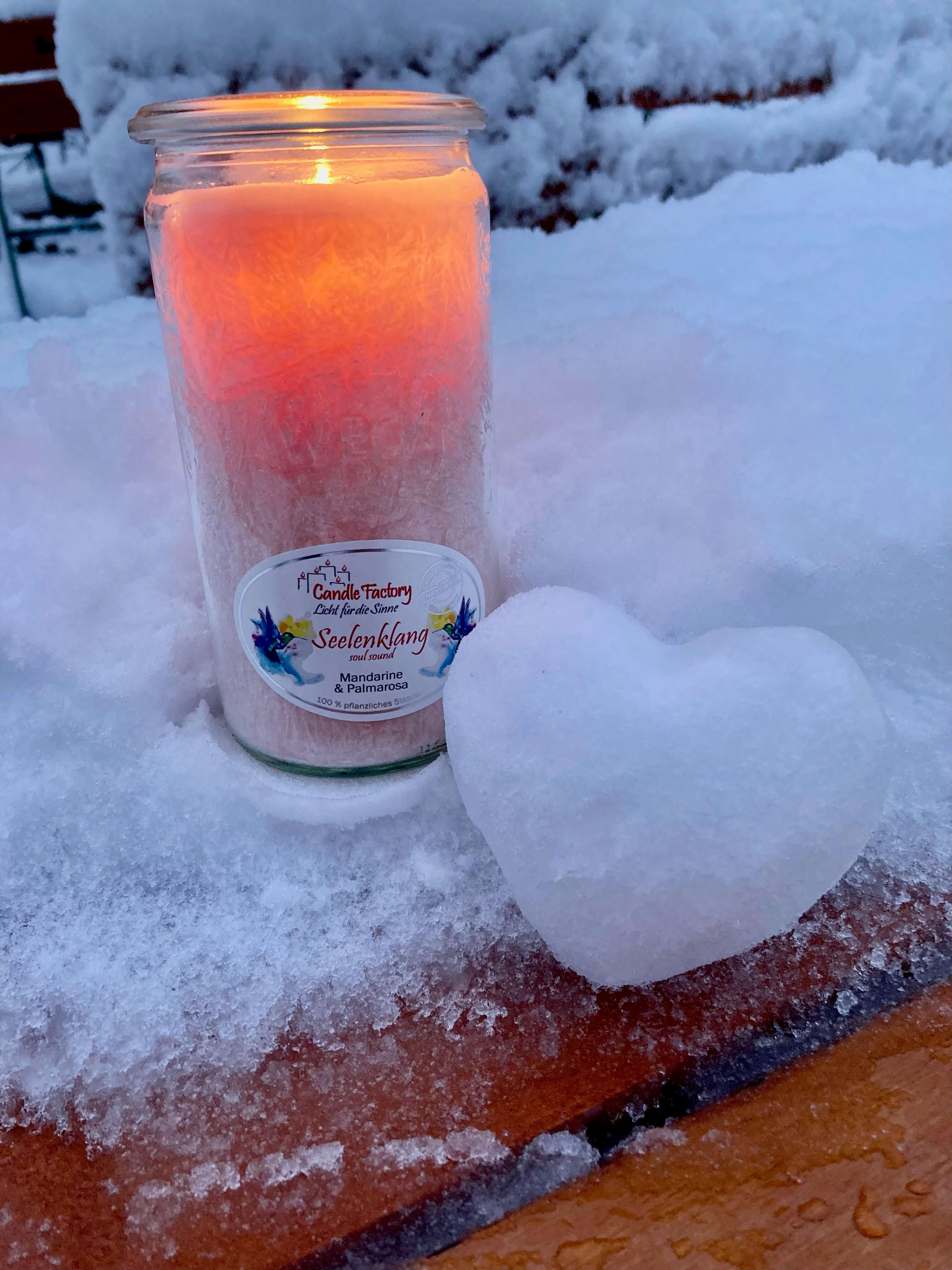 Brennende Kerze im Schnee mit einem aus Schnee geformten Herz
