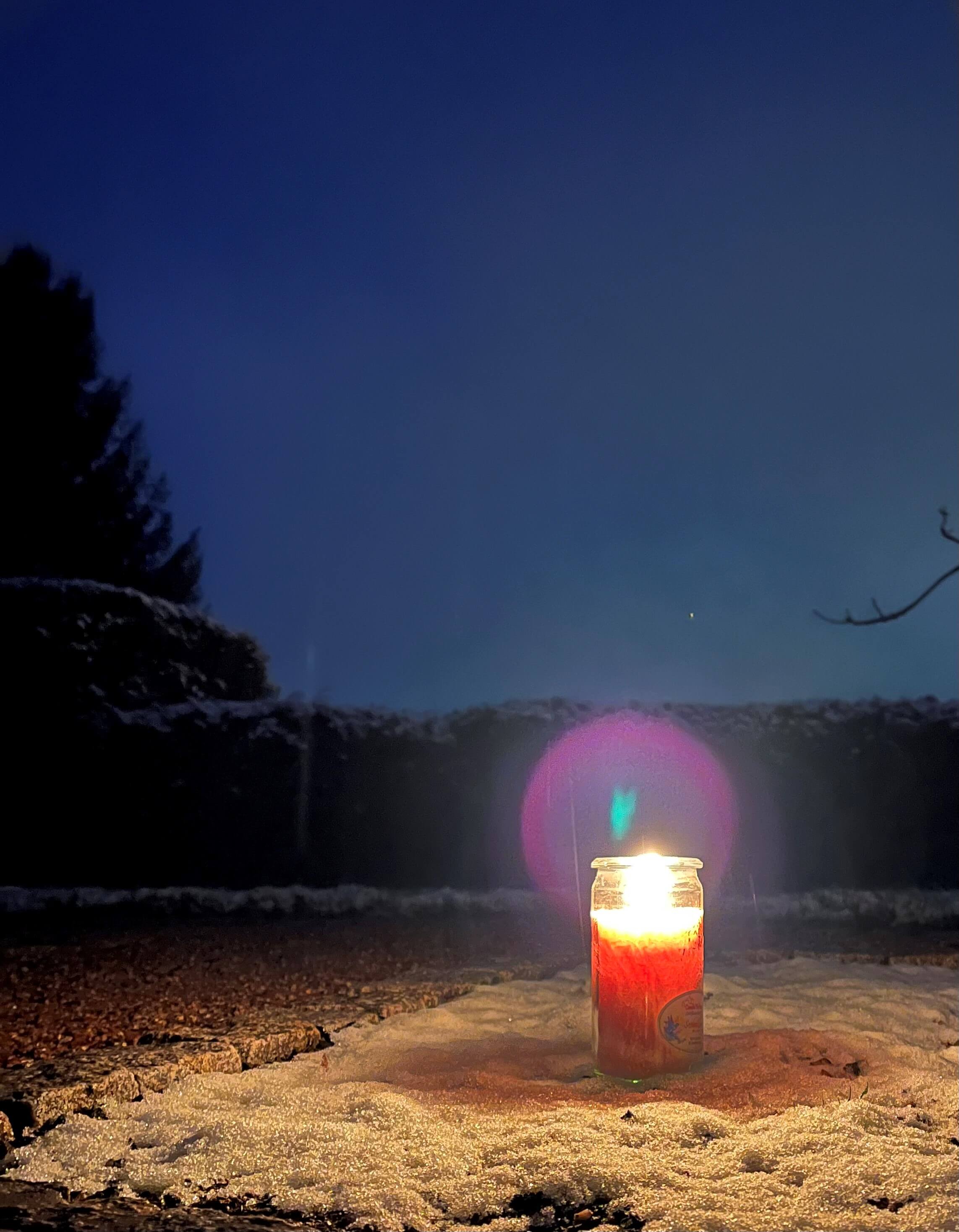 Brennende Kerze im Schnee vor dem Nachthimmel