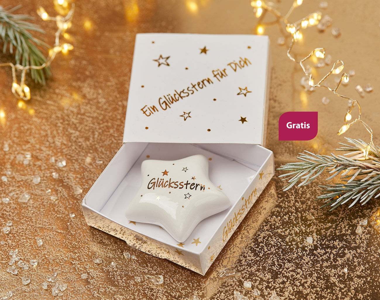 Ein kleiner fünfzackiger Stern aus weißem Porzellan mit goldener Aufschrift "Glücksstern". Daneben steht "Gratis".