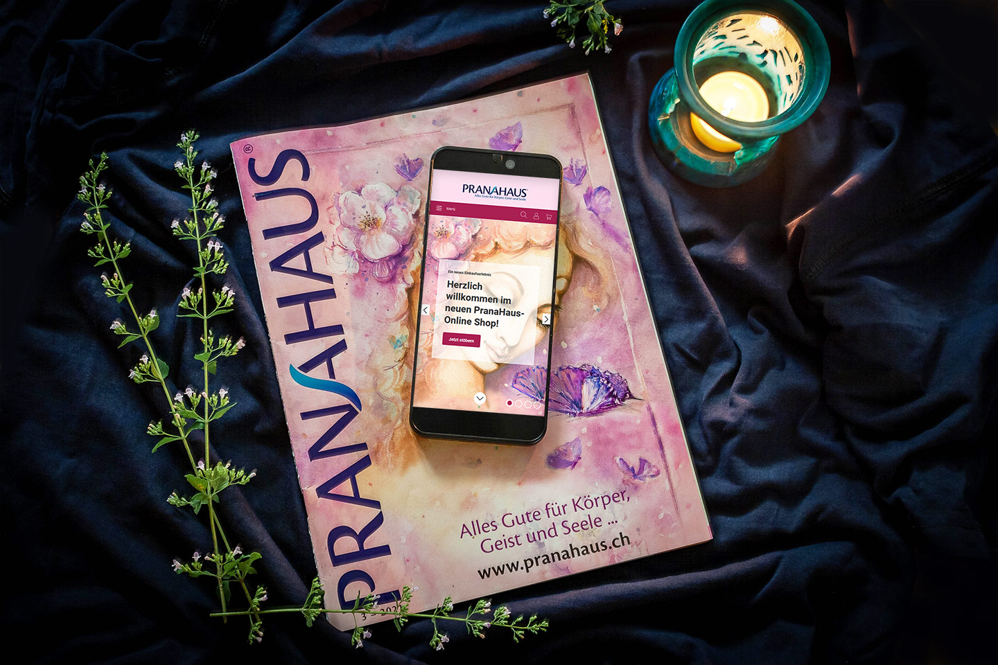 Auf dem aktuellen PranaHaus-Katalog liegt ein Smartphone, auf dem der neue PranaHaus Online-Shop zu sehen ist.