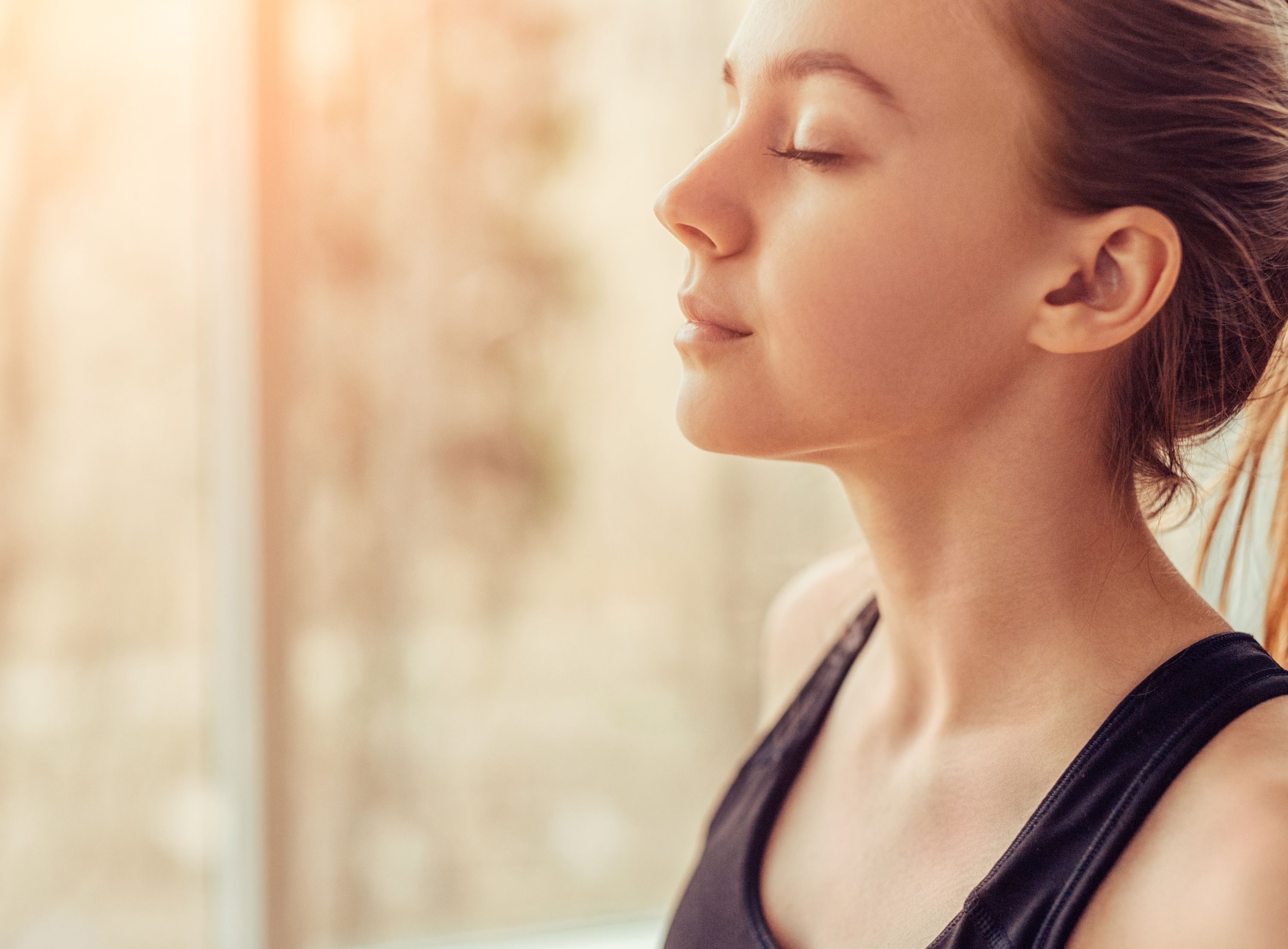 Nahaufnahme einer Frau mit geschlossenen Augen, die in warmem Licht ruhig und entspannt wirkt.