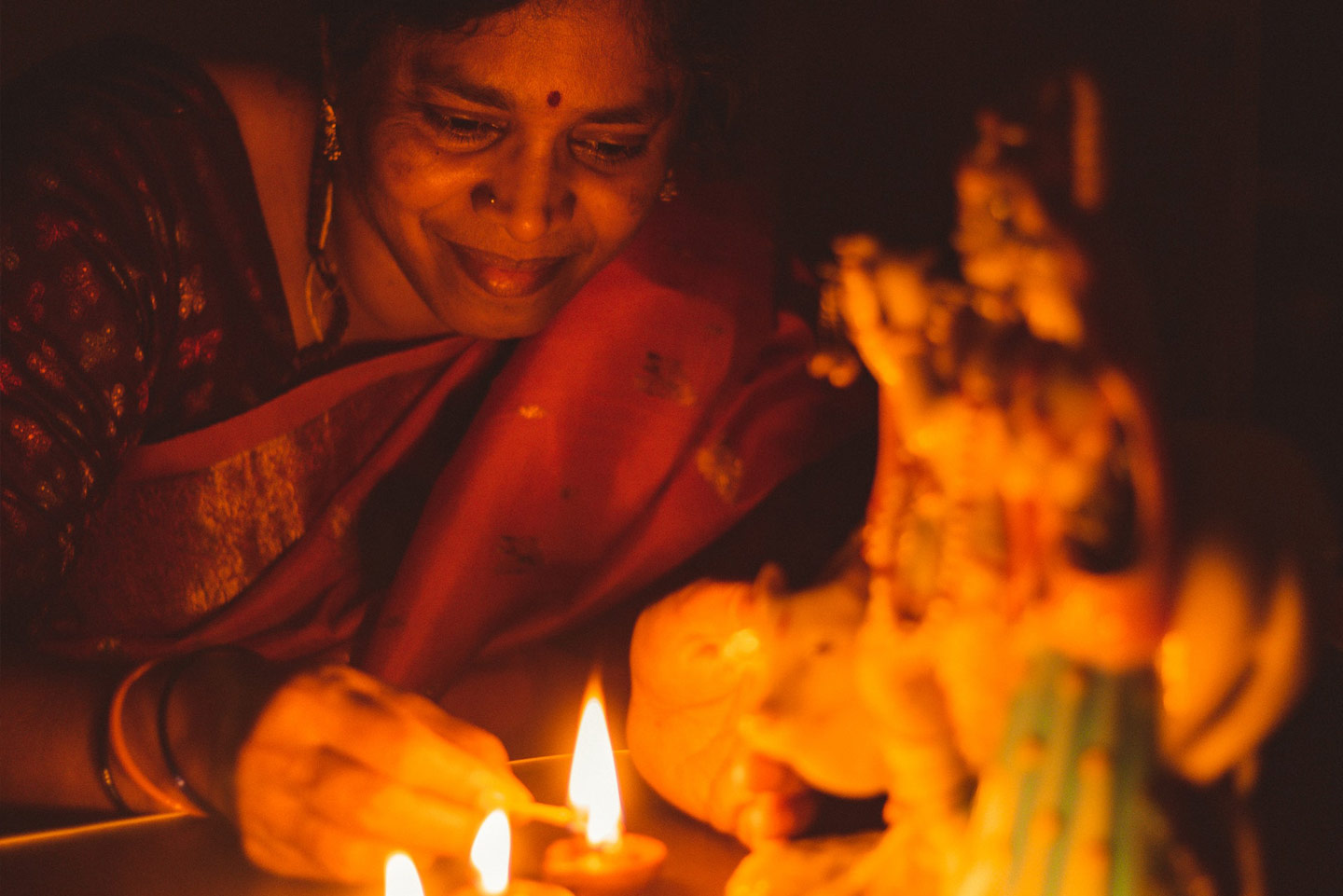 Eine indische Frau zündet vor dem Bildnis einer Gottheit lächelnd eine Kerze an