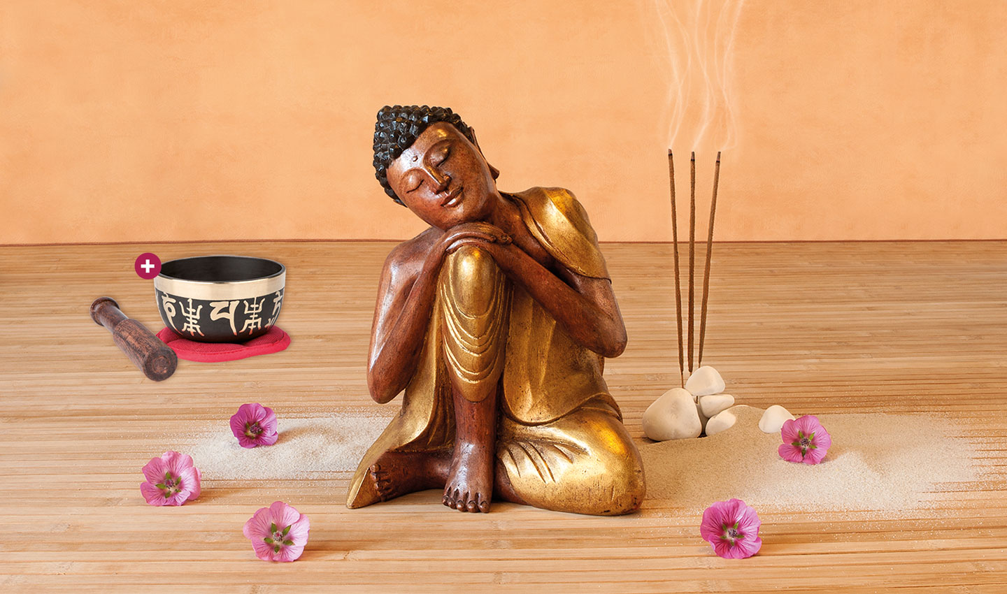 Hölzerne Buddha-Statue auf einem Holzfußboden umgeben von pinken Blumen. Daneben Räucherstäbchen und das Produkt Klangschale „OM Mani Padme Hum“