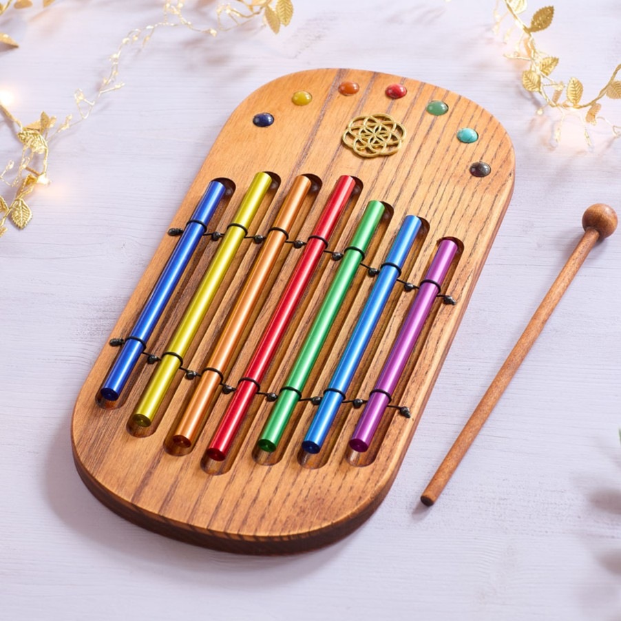 Ein kleines Holz-Klanginstrument mit acht bunten Metallstäben und einem Holzschlägel liegt auf hellem Stoff.