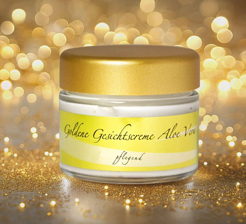 Ein Glastiegel mit goldener Gesichtscreme mit Aloe Vera steht auf einem funkelnden, goldfarbenen Untergrund.