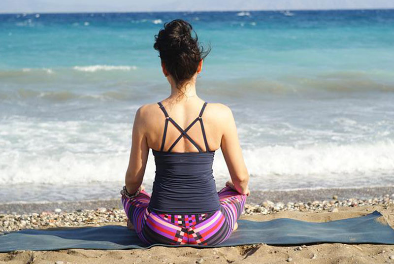 Eine Frau sitzt am Strand auf einer Yogamatte.