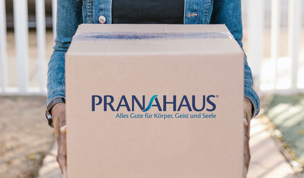 Eine Person hält ein Paket mit dem PranaHaus-Logo in Richtung der Kamera.