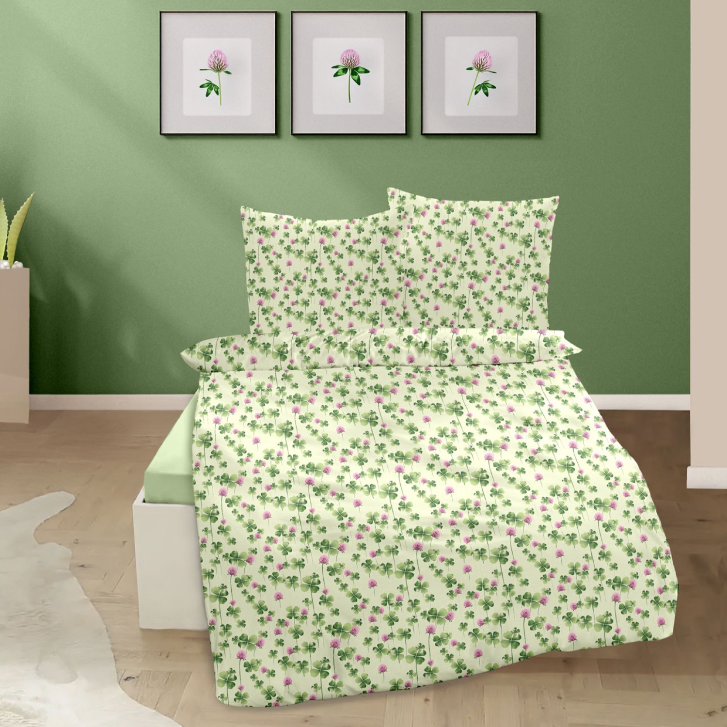 Ein Bett mit weiß-grüner Bettwäsche im Klee- und Blütenmuster steht vor einer grünen Wand mit drei gerahmten Blumenbildern darüber.