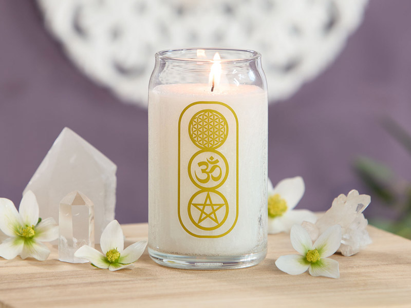 Weiße Kerze im Glas mit goldenen spirituellen Symbolen: Blume des Lebens, OM und Pentagramm. Die Szene ist dekoriert mit Kristallen und zarten weißen Blüten.