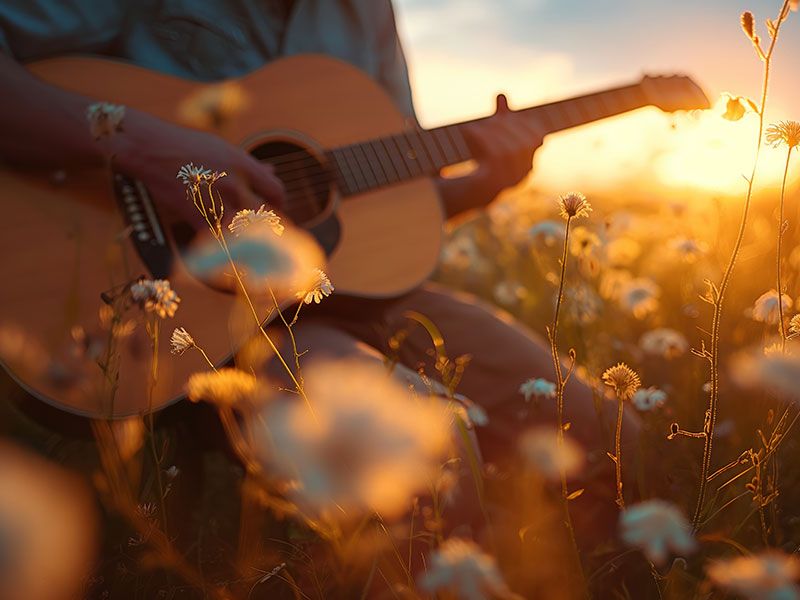 Eine Person spielt Gitarre in der Natur, im Hintergrund goldenes Sonnenlicht