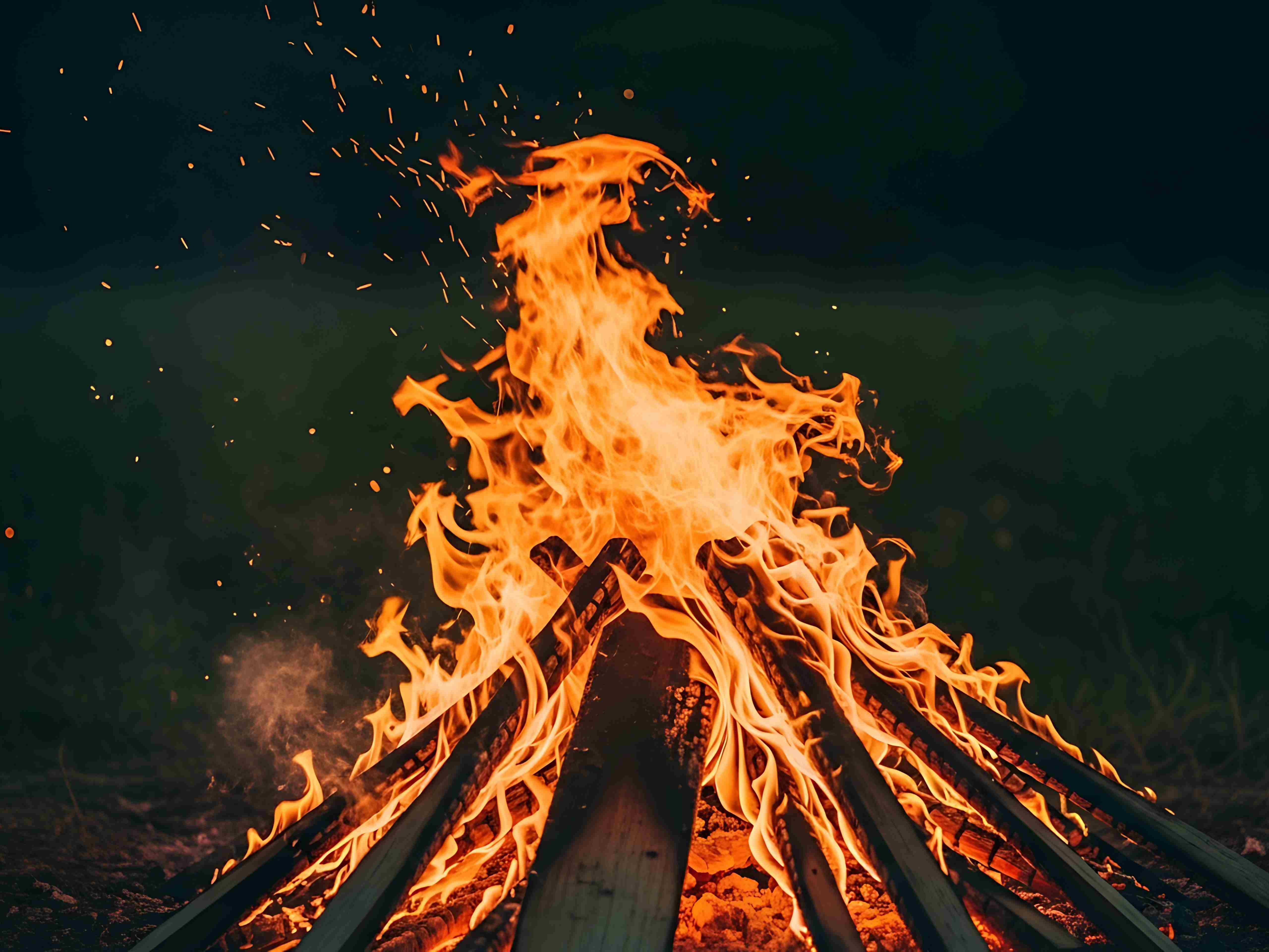 Loderndes Lagerfeuer aus aufgeschichteten Holzscheiten vor dunklem Hintergrund, mit aufsteigenden Funken.