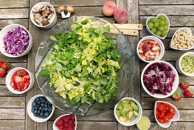 Eine große Schüssel mit grünem Salat umgeben von vielen kleinen Schüsseln mit verschiedener Rohkost.