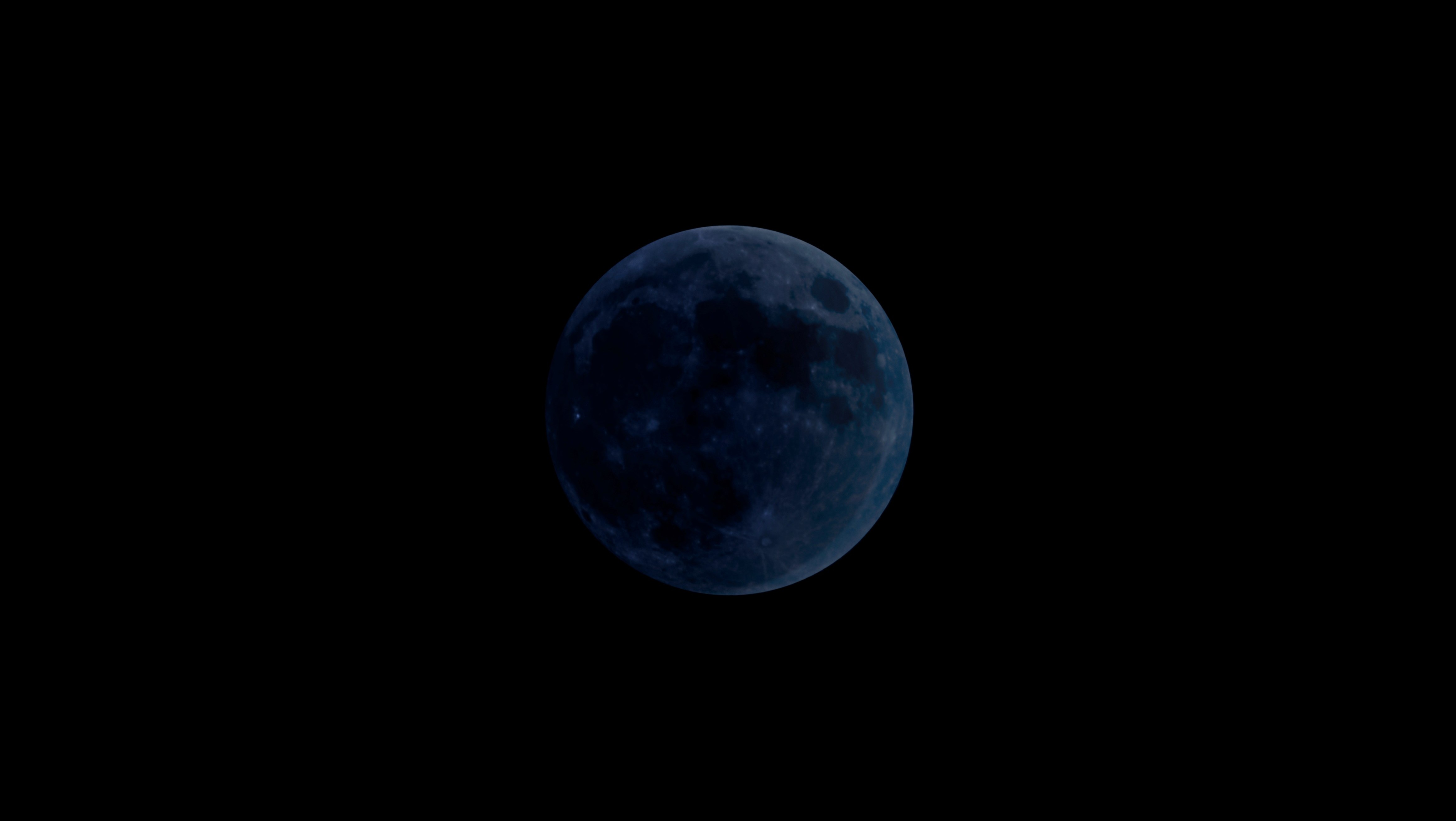 Ein dunkler Neumond vor schwarzem Nachthimmel, nur schemenhaft erkennbar.