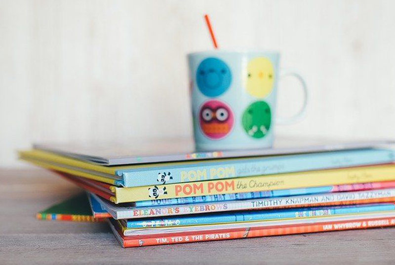 Auf einem Stapel Kinderbücher steht eine bunte Tasse.