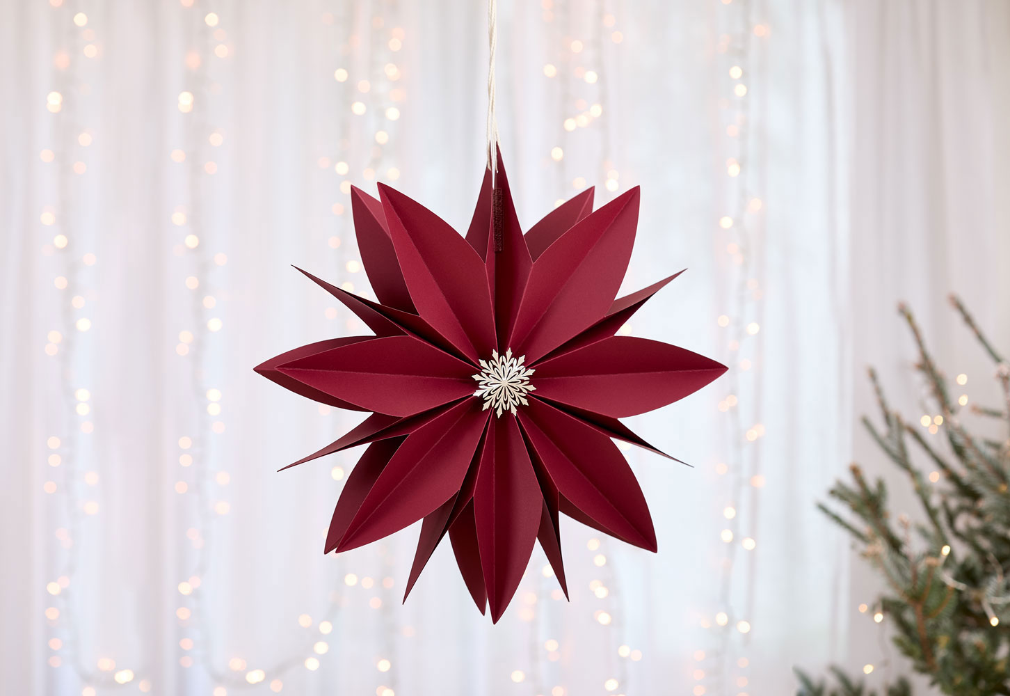 Dekorativer Weihnachtsstern in tiefem Bordeauxrot aus festem Papier, kunstvoll gefaltet zu einer stilisierten Blüte mit spitz zulaufenden Blättern. 